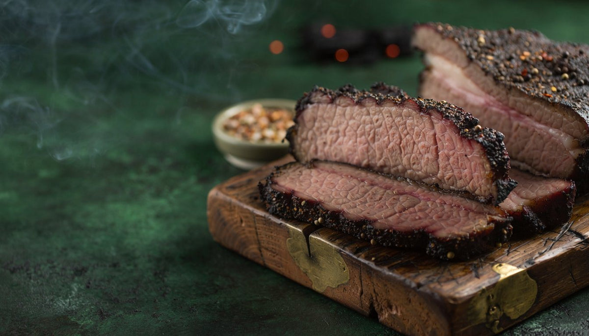 Thick slices of smoked brisket with a black, pepper-flecked bark on a rustic wooden board, a small bowl of whole spices behind and wisps of smoke against a dark green background