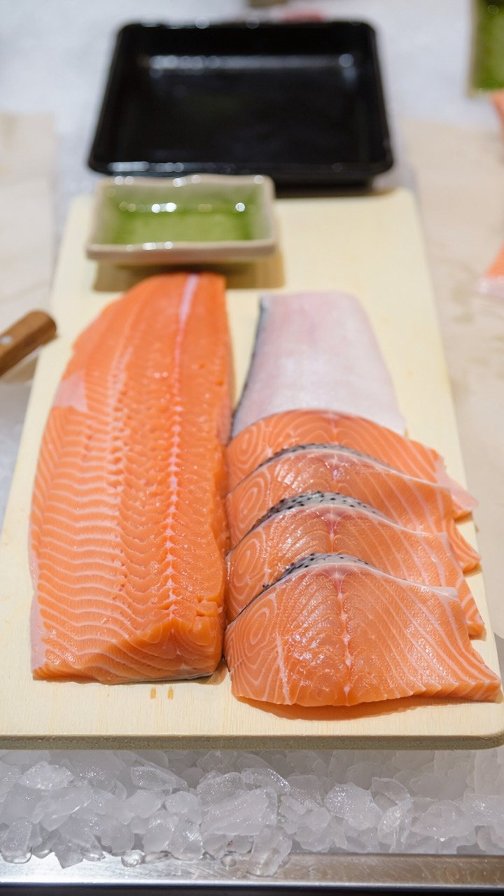 A skinless salmon loin on a pale wooden board beside thick fanned slices, with crushed ice beneath the board
