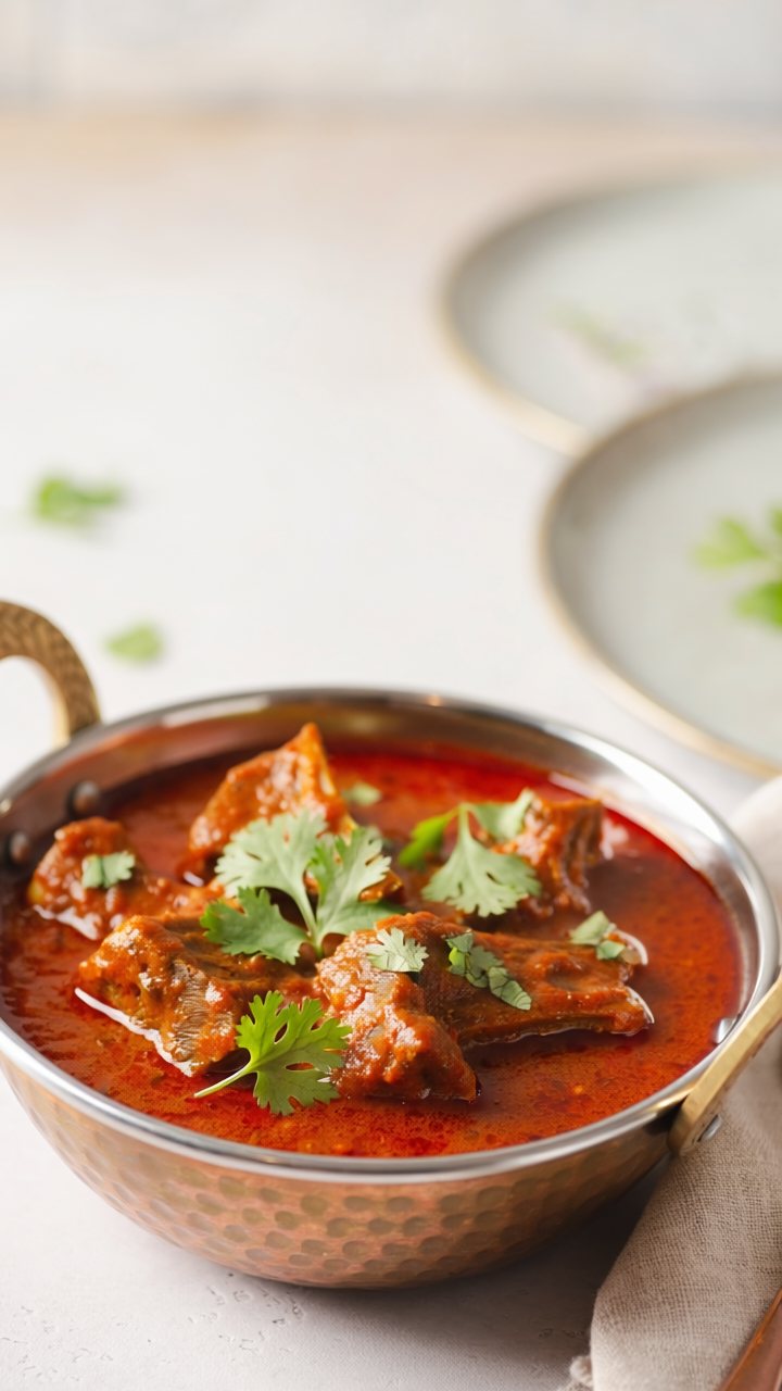 Lamb rogan josh in a deep red sauce, served in a hammered copper bowl with fresh coriander leaves.